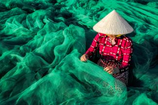 Vietnamesisches Frau näht an einem Fischnetz