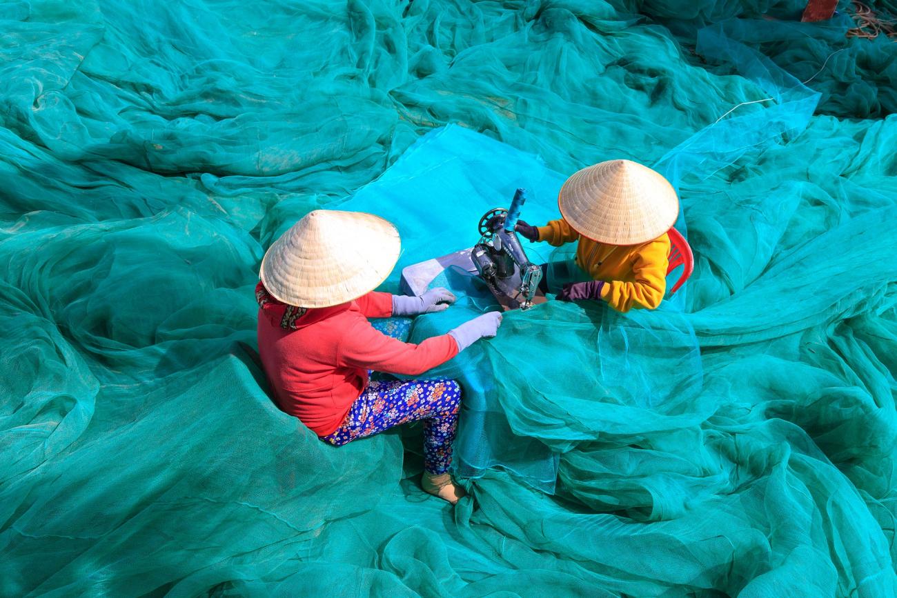 Two vietnamese women sewing a blue fish net