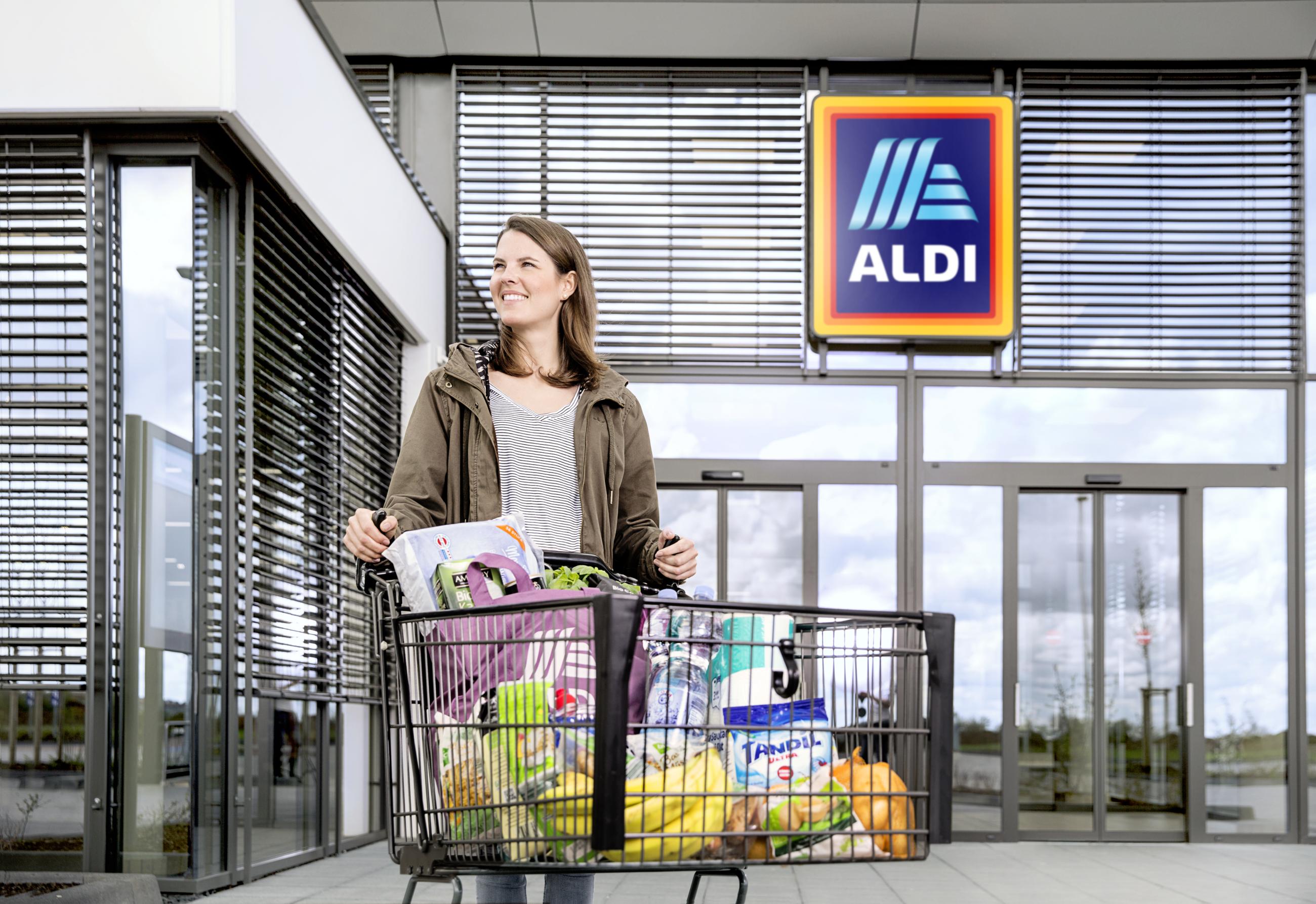 Woman with full shopping cart in front of ALDI store.
