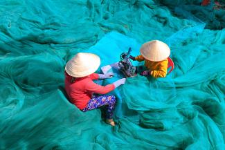 Zwei vietnamesische Frauen nähen an einem blauen Fischnetz